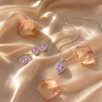 Set Trilogía Corazón de Cristal en flat-lay sobre seda color champán con pétalos de rosa