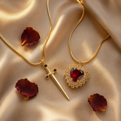 Cadenas Pareja Corazón y Espada doradas en flat-lay sobre seda champán con pétalos